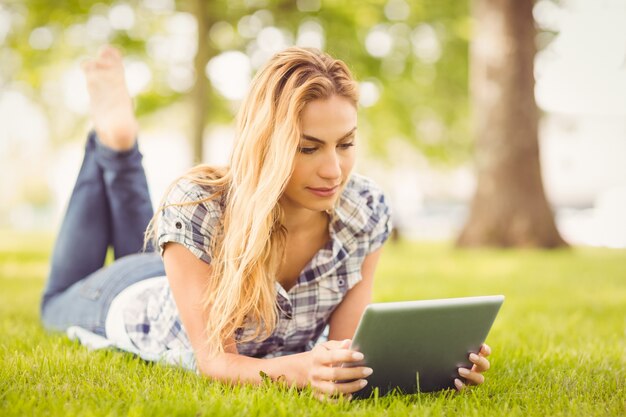 Frau, die digitale Tablette beim Lügen auf Gras verwendet