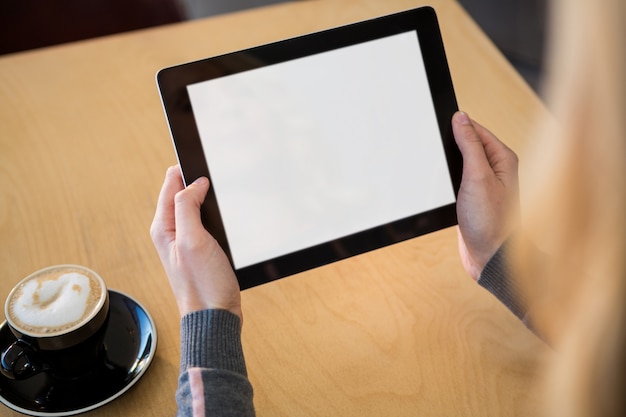 Frau, die digitale Tablette mit Tasse Kaffee auf Tisch verwendet