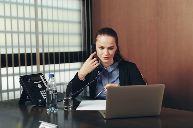 Frau, die durch die Tabelle mit Laptop im Büro sitzt