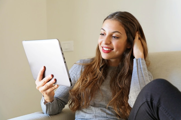 Frau, die e-book auf ihrem tablet-computer liest, sitzt auf einer couch zu hause