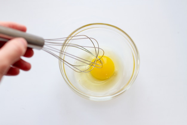 Frau, die Eier in Glasschüssel mit Schneebesen peitscht.