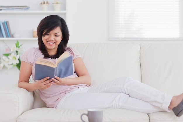 Frau, die ein Buch beim Lügen auf einem Sofa liest