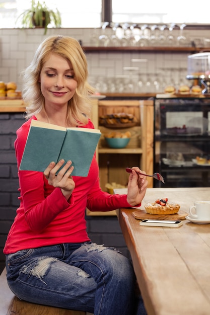 Frau, die ein Buch liest und einen Kuchen isst