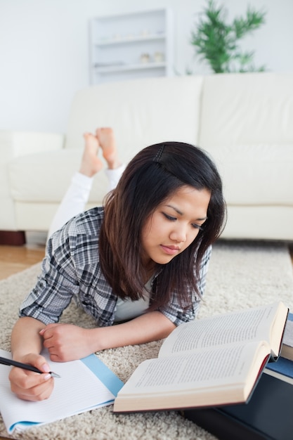 Frau, die ein Buch liest, während sie auf ein Notizbuch schreibt