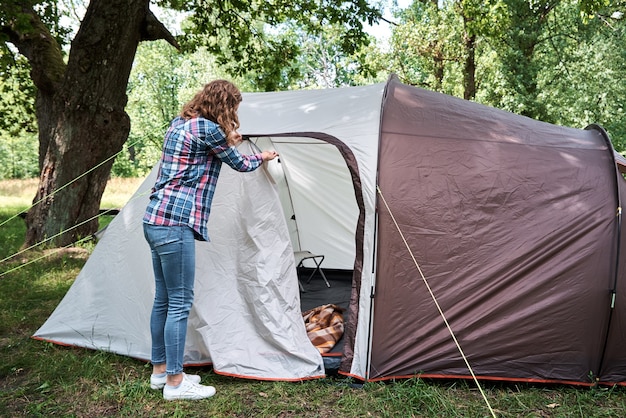 Frau, die ein Campingzelt am Wald aufbaut