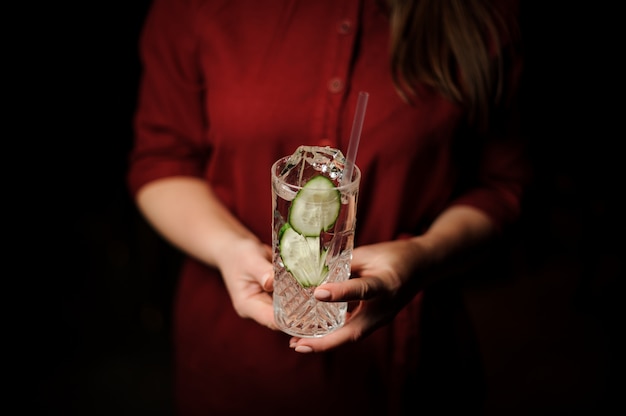 Frau, die ein Cocktailglas mit neuem alkoholischem Getränk mit Gurkenscheiben und Gin hält