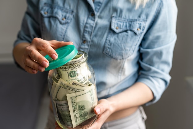 frau, die ein durchsichtiges glas voller amerikanischer dollar hält. Einkaufskonzept.