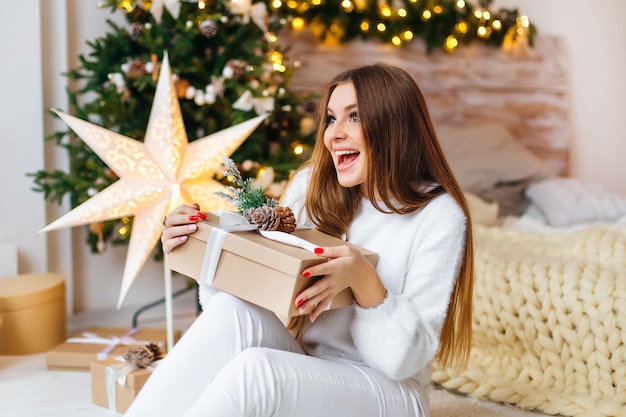 Frau, die ein Geschenk in einem gemütlichen Zimmer hält Kalter Tag in einem warmen Haus Frohe Weihnachten