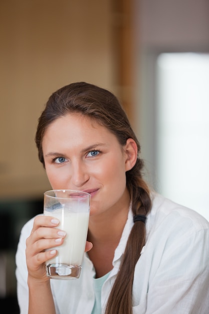 Frau, die ein Glas Milch beim Schauen der Kamera trinkt