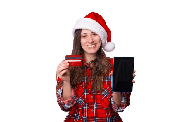 Frau, die ein kariertes Hemd und eine Weihnachtsmütze trägt, hält eine Karte und ein Tablet.