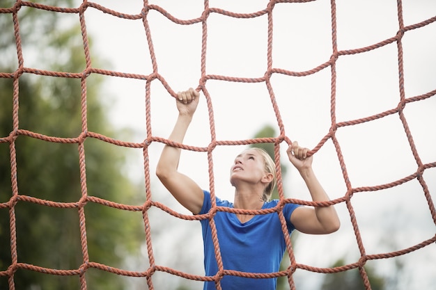 Frau, die ein Netz während des Hindernislaufs im Bootcamp klettert