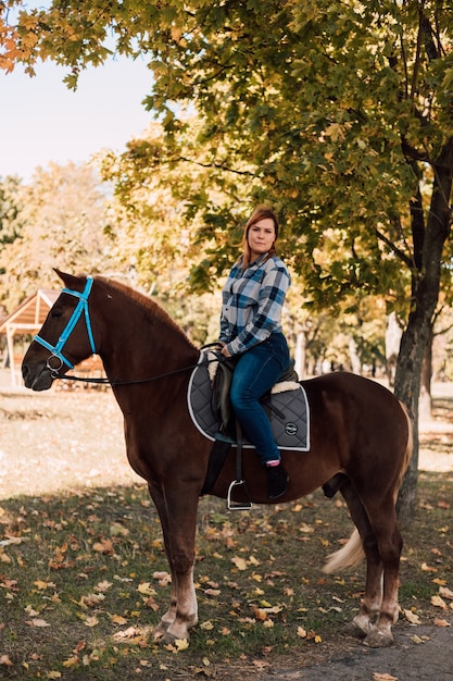 Frau, die ein Pferd reitet, das im Herbstpark spazieren geht