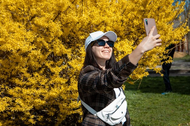 Frau, die ein Selfie-Foto vor einem gelb blühenden Busch-Kopienraum macht