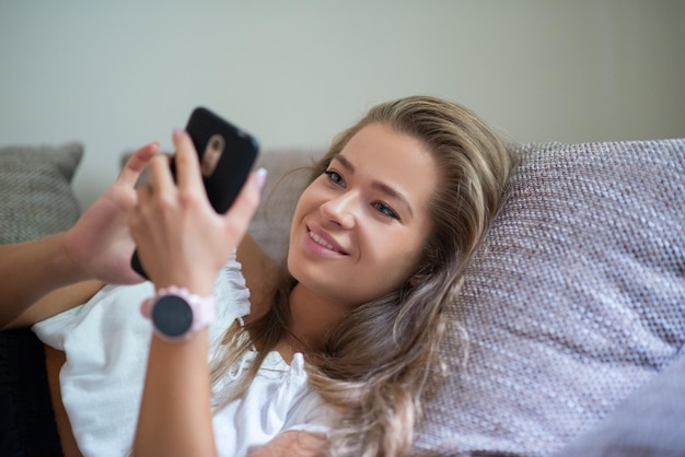 Frau, die ein Smartphone benutzt, während sie sich auf der Couch entspannt