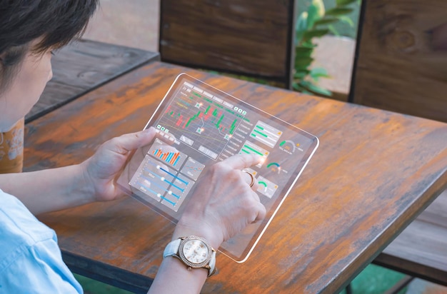 Frau, die ein transparentes digitales Tablet verwendet, um den Börsenhandel mit Finanzdaten zu überprüfen und zu analysieren
