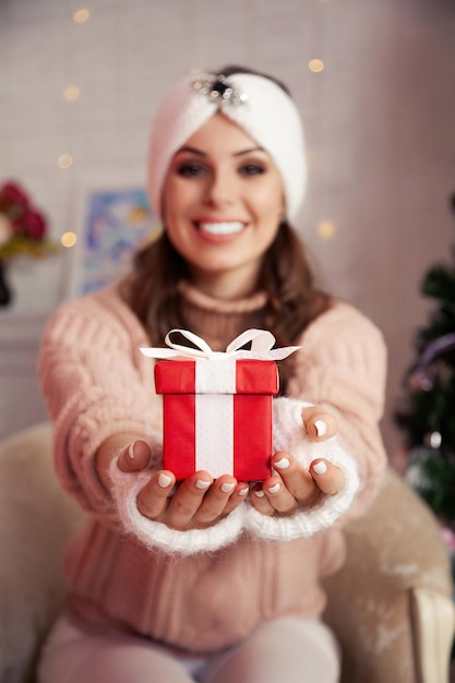 Frau, die ein Weihnachtsgeschenk hält Schöne fröhliche Frau gibt ein rotes Geschenk vor dem Hintergrund