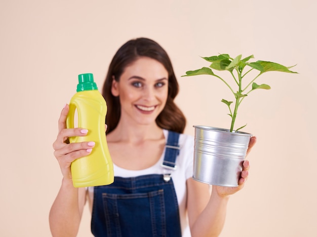 Frau, die eine Flasche chemischen Düngers und Sämling hält