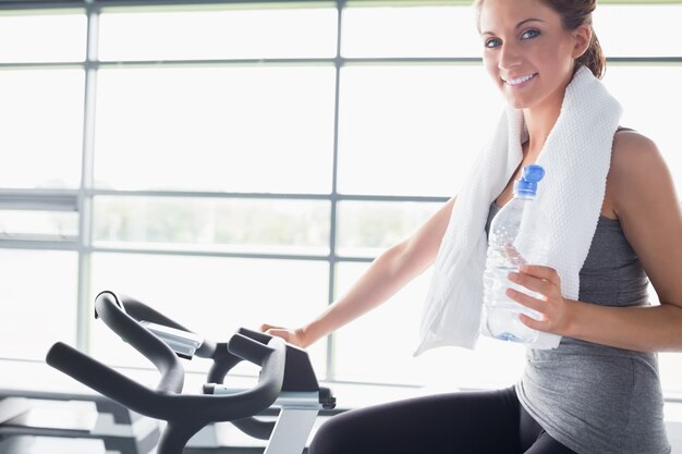 Frau, die eine Flasche hält und ein Hometrainer fährt