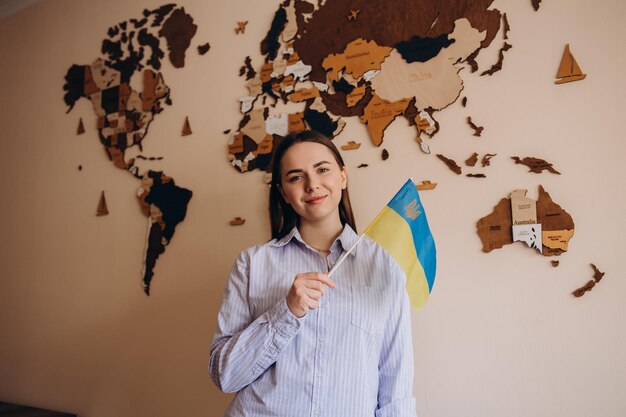 Frau, die eine gelbe und blaue Flagge der Ukraine auf einer Hintergrundweltkarte hält