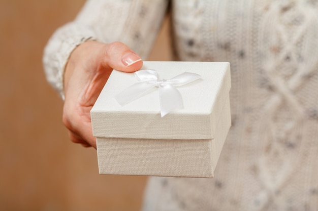 Frau, die eine Geschenkbox in der Hand hält. Geringe Schärfentiefe, selektiver Fokus auf die Box. Konzept, im Urlaub oder Geburtstag ein Geschenk zu machen.