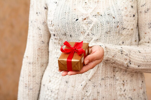 Frau, die eine Geschenkbox mit einem roten Band in der Hand hält. Geringe Schärfentiefe, selektiver Fokus auf die Box. Konzept, im Urlaub oder Geburtstag ein Geschenk zu machen.