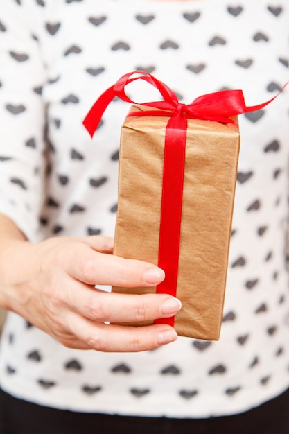 Foto frau, die eine geschenkbox mit einem roten band in der hand hält. geringe schärfentiefe, selektiver fokus auf die box. konzept, im urlaub oder geburtstag ein geschenk zu machen.