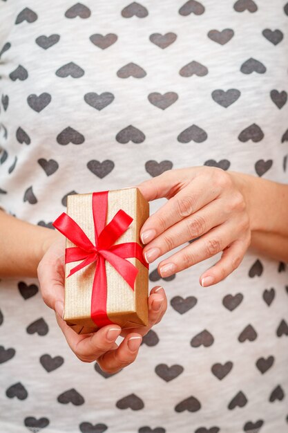 Frau, die eine Geschenkbox mit einem roten Band in ihren Händen hält. Geringe Schärfentiefe, selektiver Fokus auf die Box. Konzept, im Urlaub ein Geschenk zu machen.