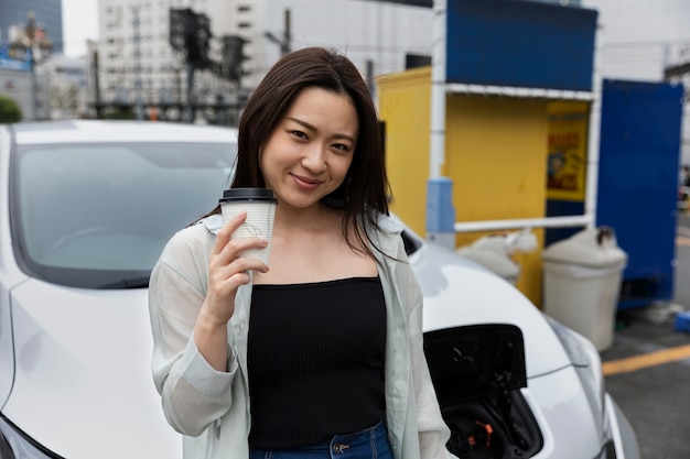 Foto frau, die eine kaffeepause macht, während ihr elektroauto auflädt