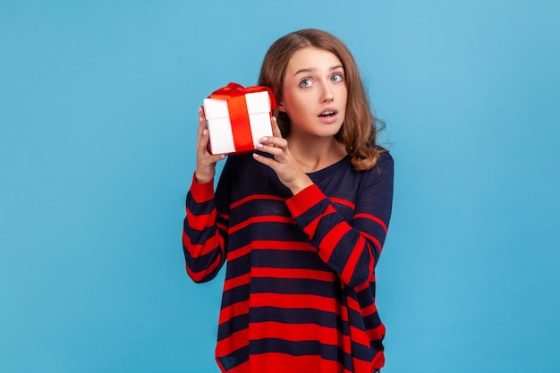 Foto frau, die eine schüttelnde geschenkbox mit neugierigem gesichtsausdruck hält, will wissen, was drin ist