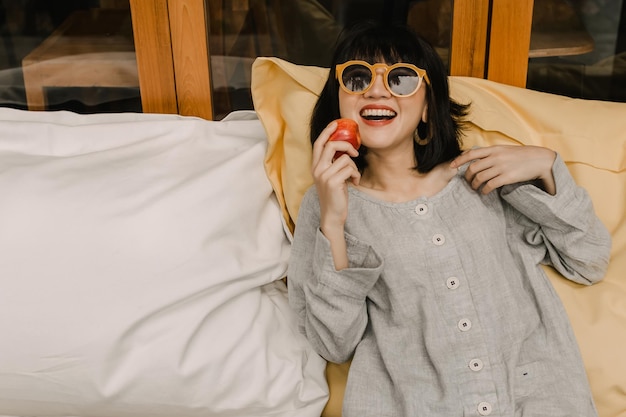 Foto frau, die eine sonnenbrille trägt, isst apfel frau hält apfel