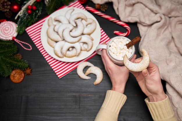 Frau, die eine Tasse Kakao mit Marshmallow und Vanillekipferl-Vanille-Kipferl-Keksen auf einem Teller hält