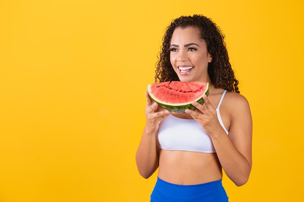 Frau, die eine Wassermelone auf gelbem Hintergrund beißt.