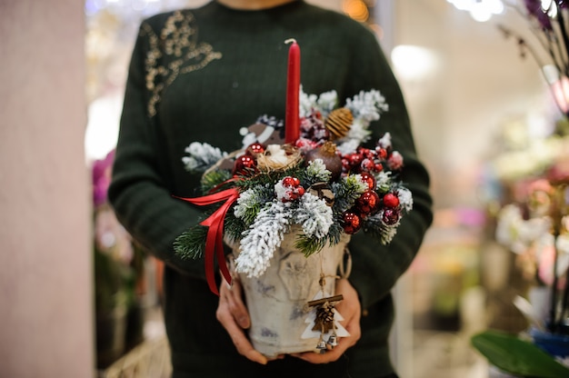 Frau, die eine Weihnachtskomposition aus Tannenbaum, Glaskugeln, Zapfen, Schnee und Kerze hält