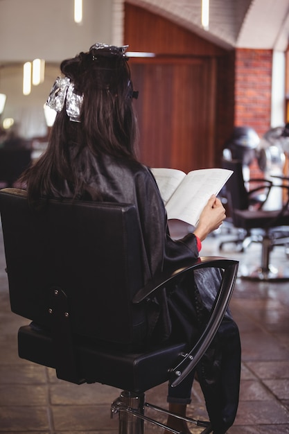 Frau, die eine Zeitschrift liest, während sie mit Haarfärbemitteln in ihrem Kopf wartet