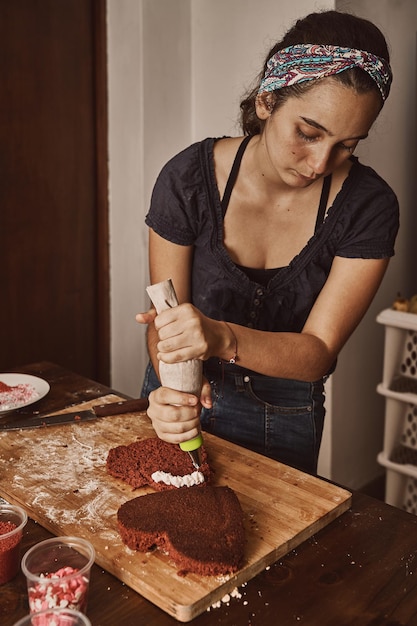 Frau, die einem roten Samtkuchen Frischkäse-Zuckerguss hinzufügt