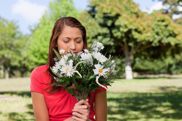 Frau, die einen Blumenstrauß bei der Stellung in einem Park riecht