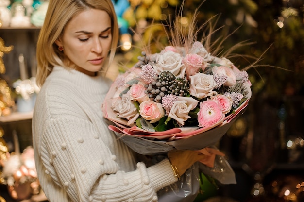 Frau, die einen Blumenstrauß der rosa und beige Farbrosen mit einem Dekor hält