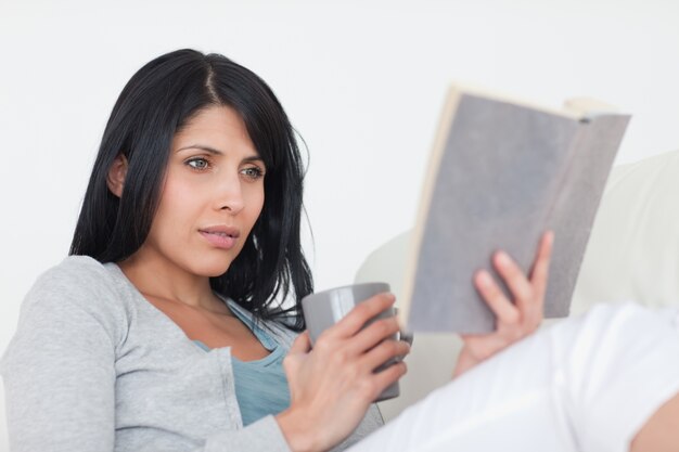 Frau, die einen grauen Becher beim Lesen eines Buches hält