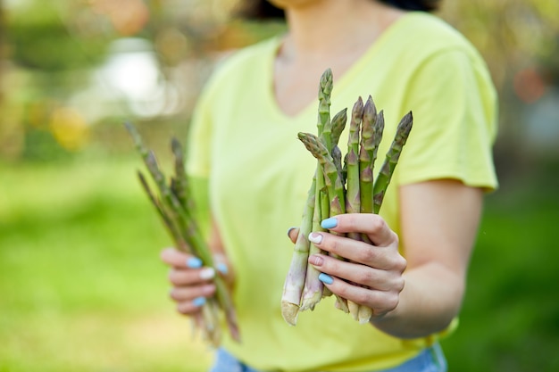 Frau, die einen Haufen grünen Spargels in den Händen im Freien hält, Spears of Fresh green Spargel in der Sonne, Platz für Text kopieren. Ernte, kochfertig, gesunde vegane Ernährung, lokales Essen.