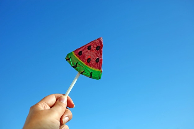 Frau, die einen klaren Wassermelonenlutscher gegen hellen blauen Himmel hält