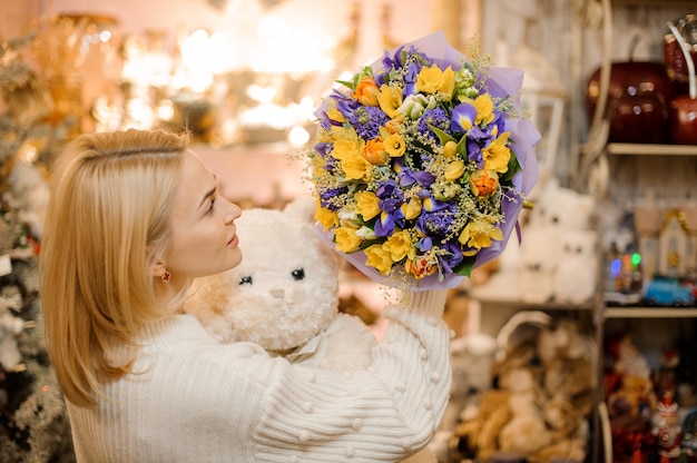 Frau, die einen kleinen Blumenstrauß mit lila und weißen Blumen hält, die in Geschenkpapier eingewickelt werden