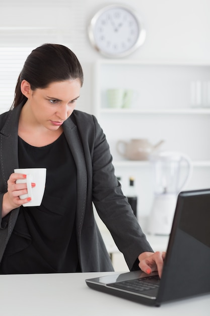 Frau, die einen Laptop beim Anhalten eines Bechers betrachtet