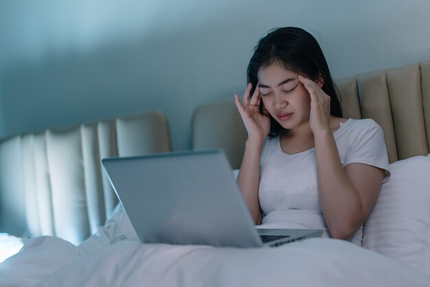 Frau, die einen Laptop benutzt und auf Bett liegt