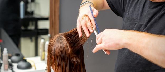 Frau, die einen neuen Haarschnitt hat. Männlicher Friseur, der in einem Friseursalon braunes Haar mit einer Schere schneidet.