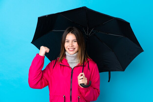 Frau, die einen Regenschirm über lokalisierter blauer Wand hält