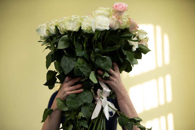 Frau, die einen riesigen Strauß weißer Rosen hält, die ihr Gesicht bedecken