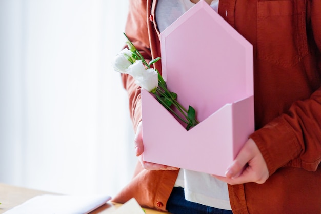 Frau, die einen rosa Umschlag mit weißen Rosen hält.