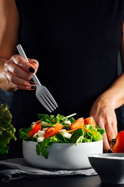 Frau, die einen Salat mit Tomaten-Salat-Olivenöl und Salzkonzept der gesunden Diät vorbereitet