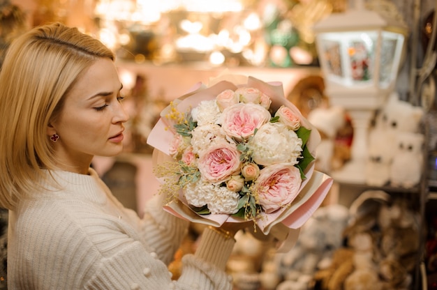 Frau, die einen Strauß zarter rosa Pfingstrosenrosen verziert, die mit kleinen Zweigen und grünen Blättern verziert sind