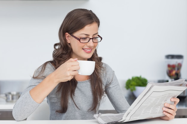 Frau, die einen Tasse Kaffee hält und eine Zeitung liest